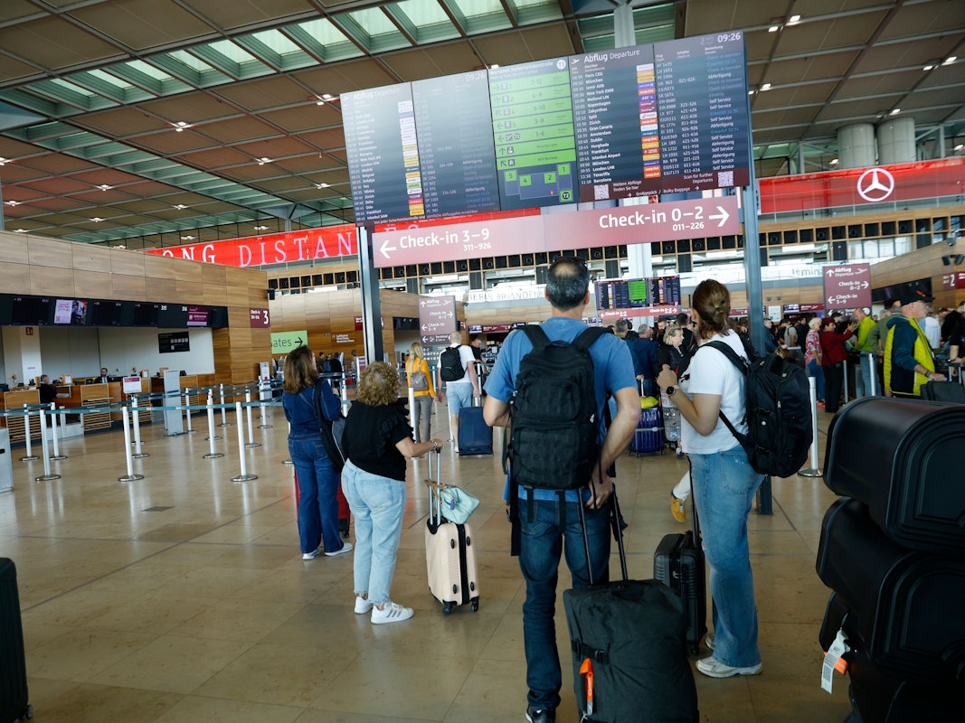 Reisende gucken auf eine Tafel am Flughafen.