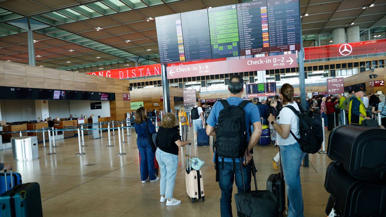 Reisende gucken auf eine Tafel am Flughafen.