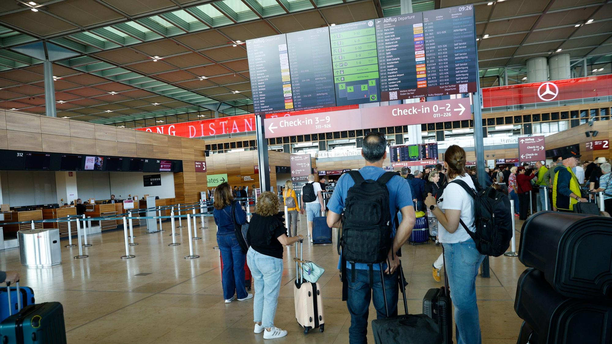Reisende gucken auf eine Tafel am Flughafen.