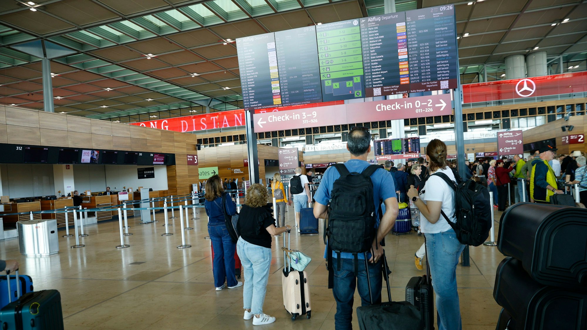 Reisende gucken auf eine Tafel am Flughafen.