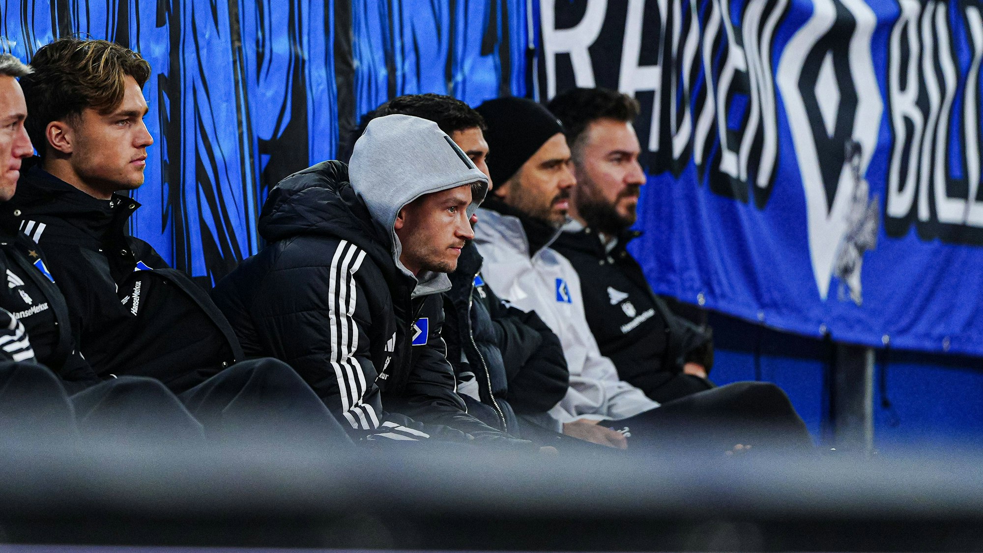 Noah Katterbach sitzt mit Kapuze auf dem Kopf auf der Ersatzbank.