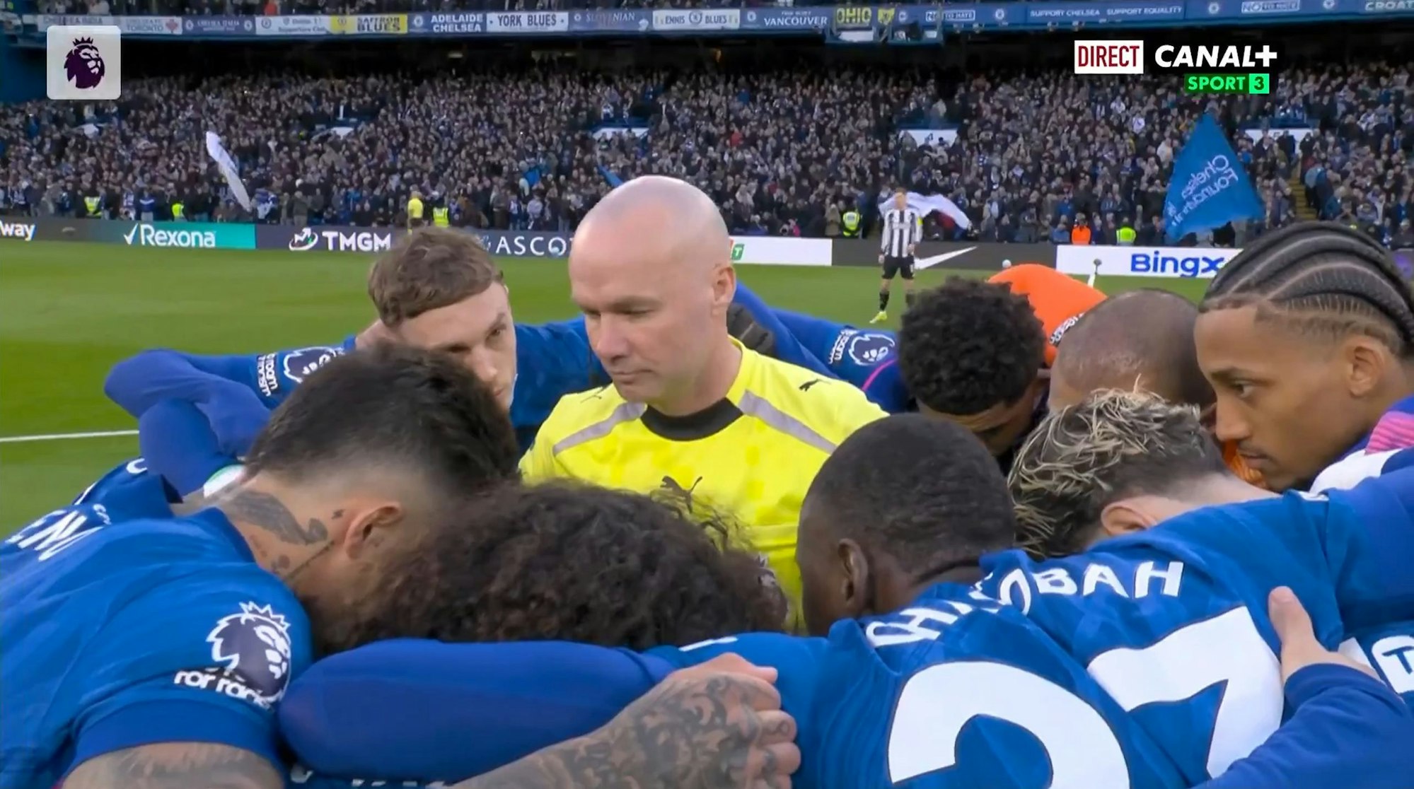 Schiedsrichter Paul Tierney steht in der Mitte des Spielerkreises vom FC Chelsea