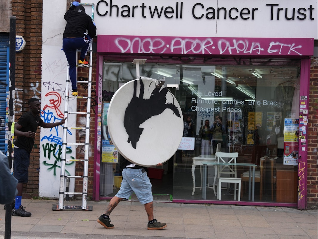 Menschen entfernen im August 2024 ein Kunstwerk von Banksy, das einen heulenden Wolf auf einer Satellitenschüssel zeigt, die auf einem Ladendach angebracht war.