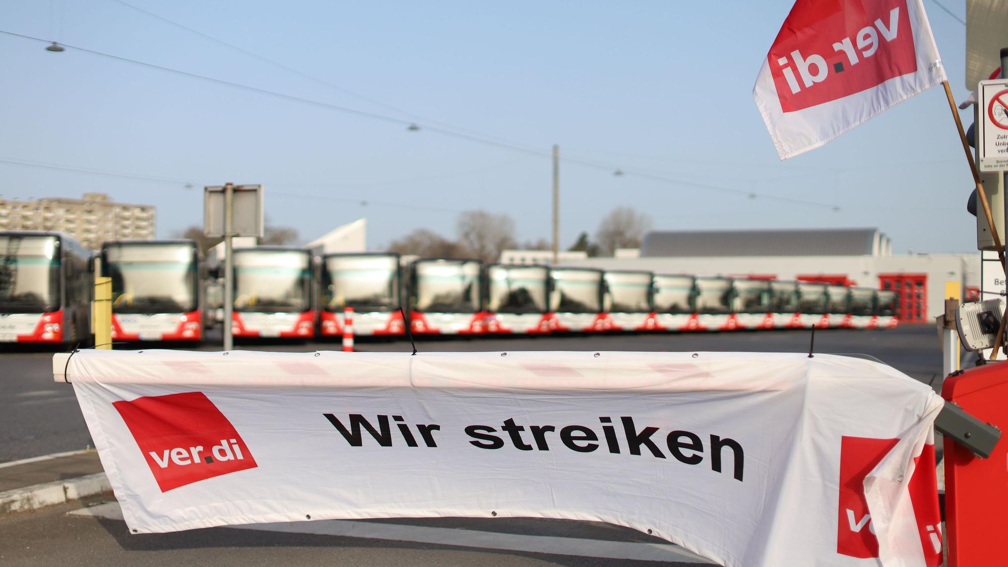 Auf einem Banner steht "Wir streiken", im Hintergrund stehen zahlreiche Busse.