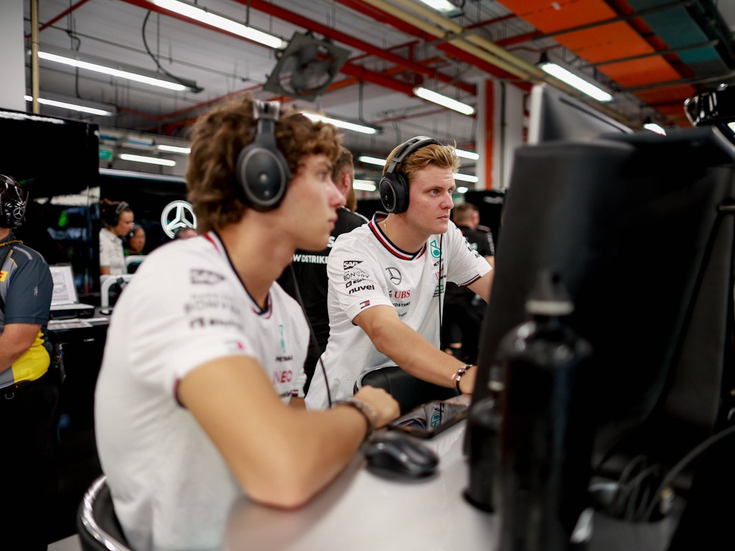 Mick Schumacher und Kimi Antonelli blicken gemeinsam auf einen Bildschirm.