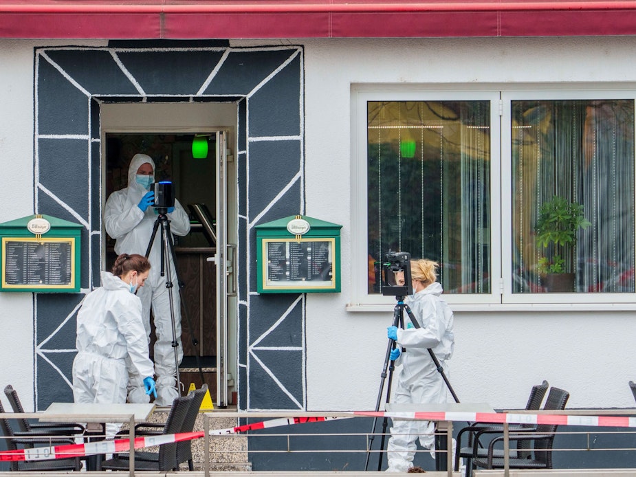 Drei Personen in weißen Schutzanzügen sichern vor sowie in der Tür eines Lokals Spuren.