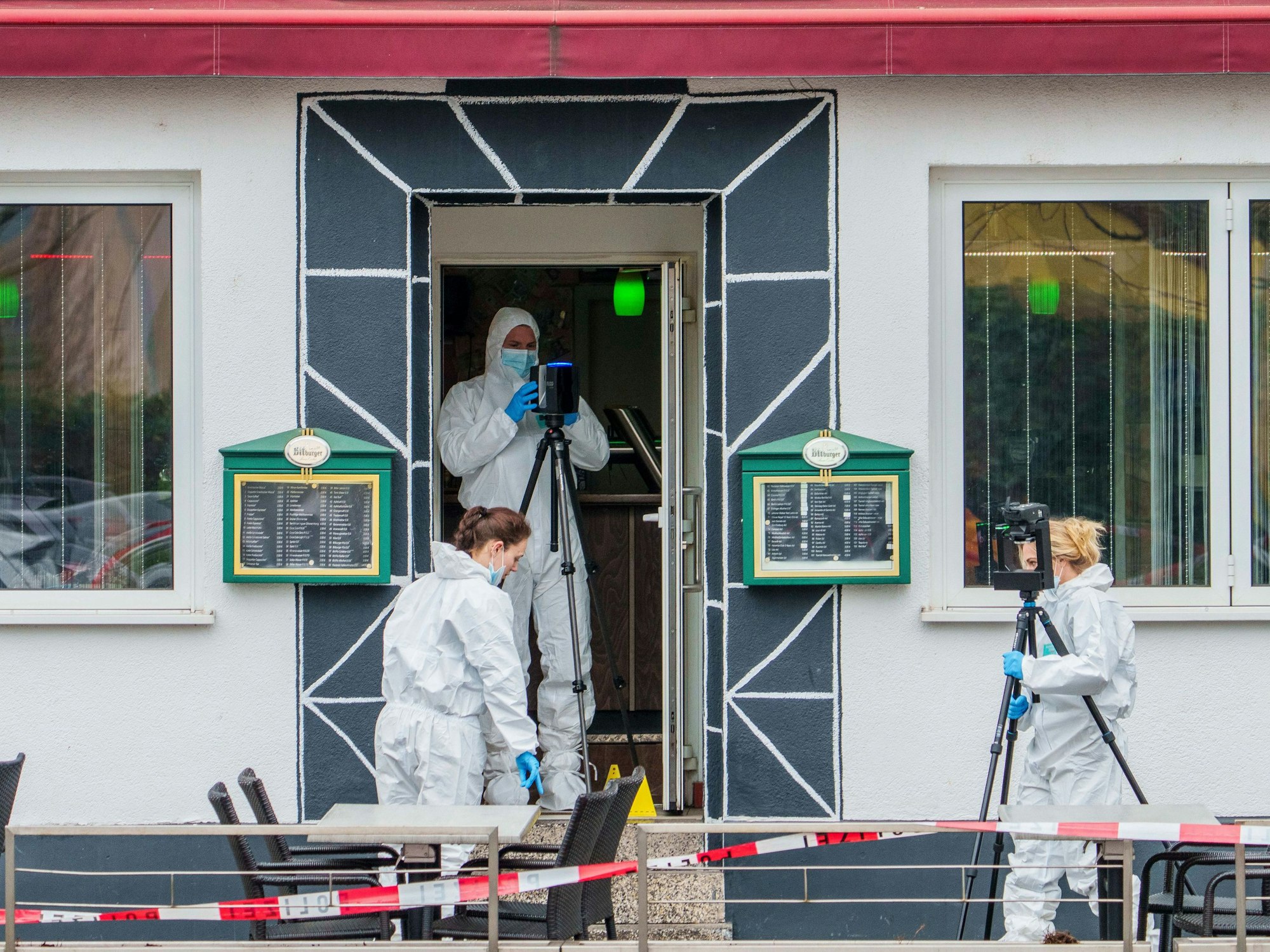 Drei Personen in weißen Schutzanzügen sichern vor sowie in der Tür eines Lokals Spuren.