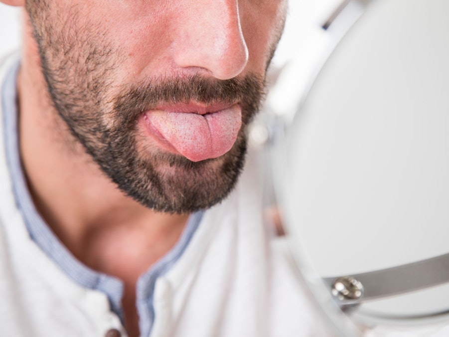 Mann betrachtet seine Zunge im Spiegel