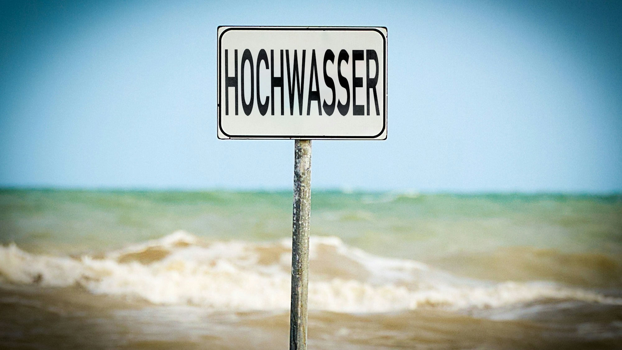 Schild mit „Hochwasser“ vor stürmischem Wasser