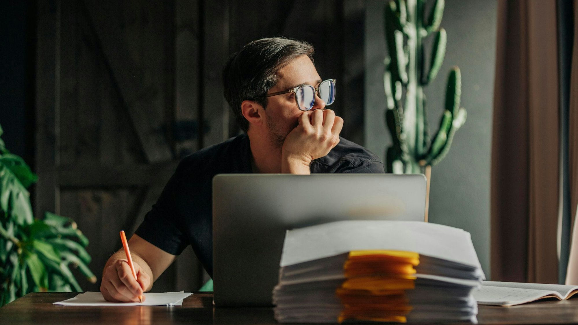 Ein Mann arbeitet am Laptop und sieht aus dem Fenster