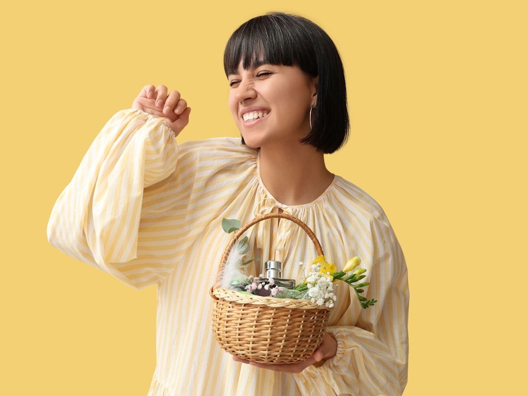 Eine junge Frau hält ein Osterkörbchen mit Parfüm gefüllt.