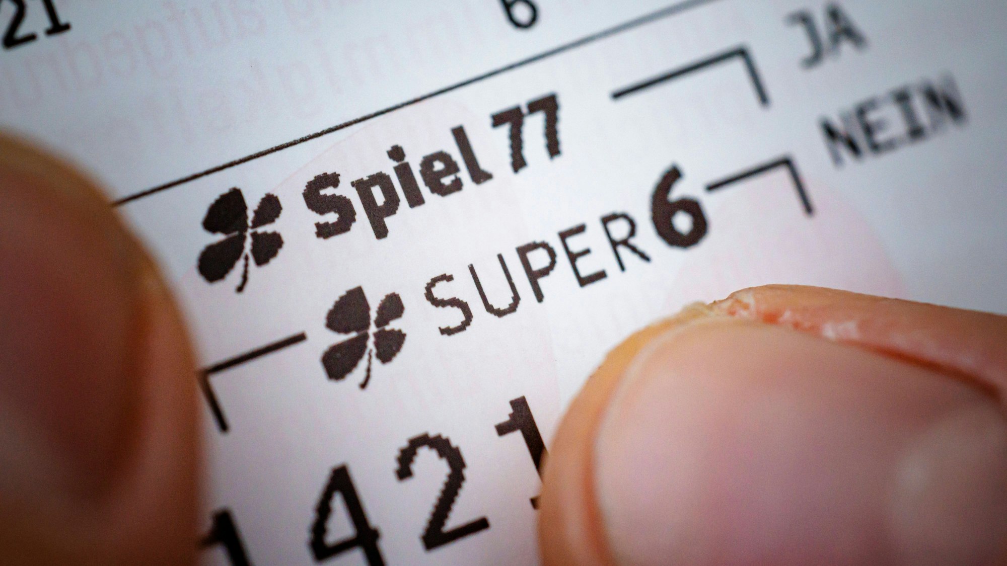 Eine Hand mit Lottoschein „Spiel 77“ und „Super 6“