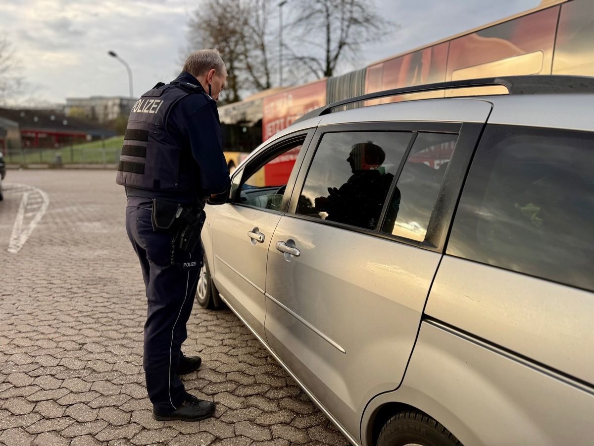 Ein Polizist oder eine Polizistin führt eine Gurtkontrolle bei einem Autofahrer oder einer Autofahrerin durch.