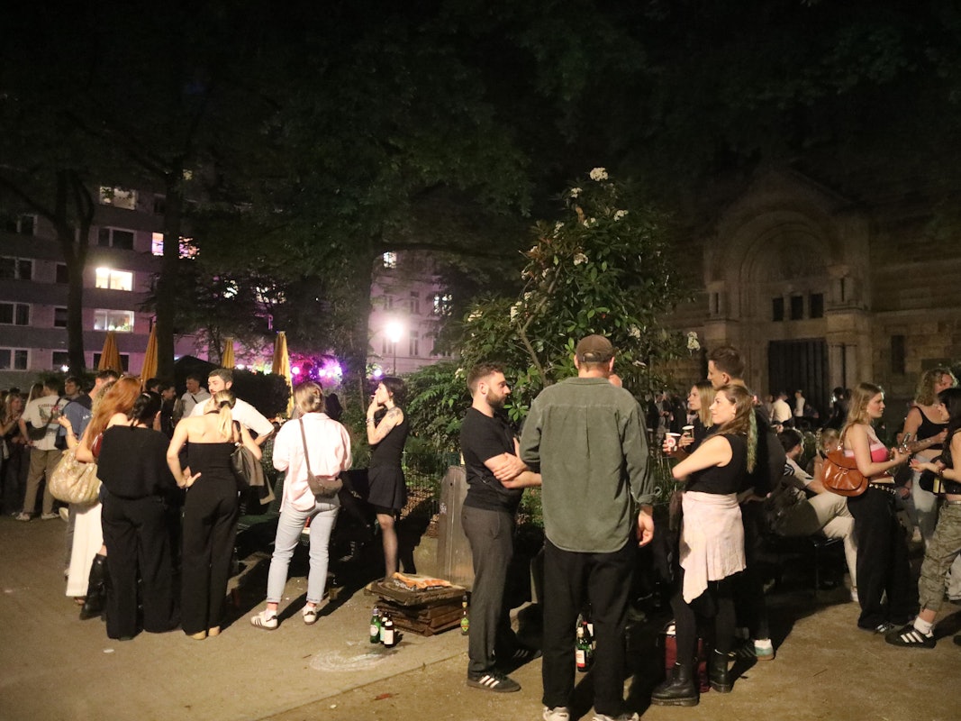 Das Bild zeigt die Situation auf dem Brüsseler Platz im April 2025: Menschen treffen und unterhalten sich, manche halten dabei ein Getränk.