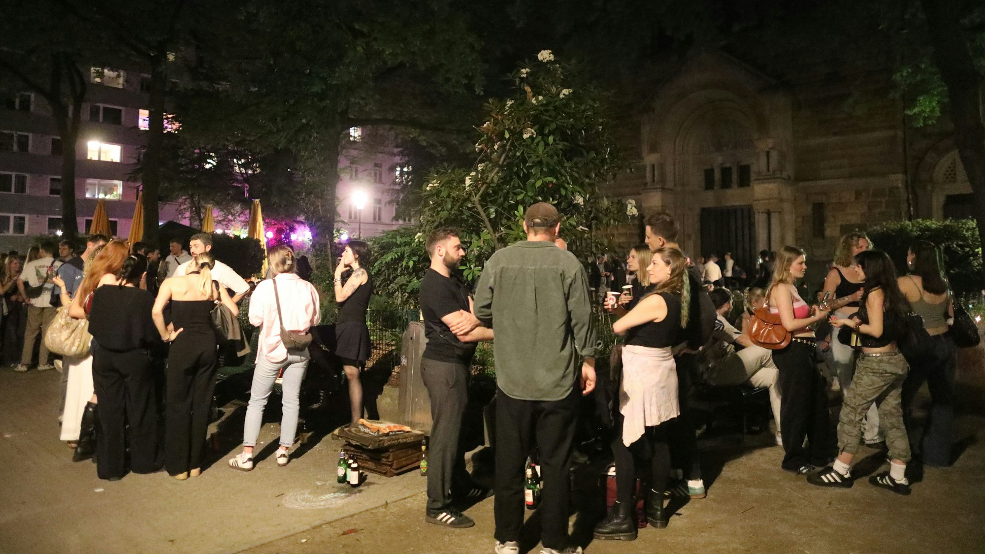 Das Bild zeigt die Situation auf dem Brüsseler Platz im April 2025: Menschen treffen und unterhalten sich, manche halten dabei ein Getränk.