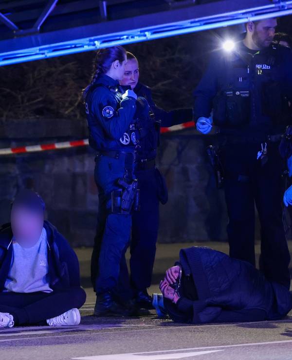 19.03.2026, Nordrhein-Westfalen, Mönchengladbach: Zwei Tatverdächtige sitzen und liegen in Handschellen gefesselt auf einer Straße, bewacht von Polizeibeamten. In der Innenstadt waren zuvor Schüsse gefallen. Es gebe Verletzte, sagte ein Polizeisprecher. Foto: Christoph Reichwein/dpa - ACHTUNG: Tatverdächtige Person wurde aus rechtlichen Gründen gepixelt +++ dpa-Bildfunk +++