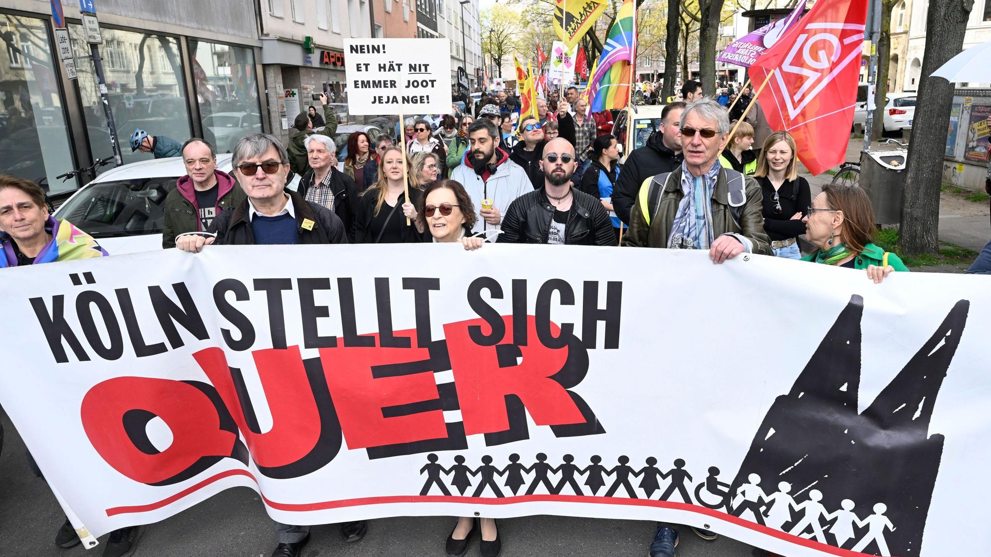 Menschen demonstrieren und halten Plakate hoch, vorweg halten mehrere Personen ein großes Banner mit der Aufschrift Köln stellt sich quer.