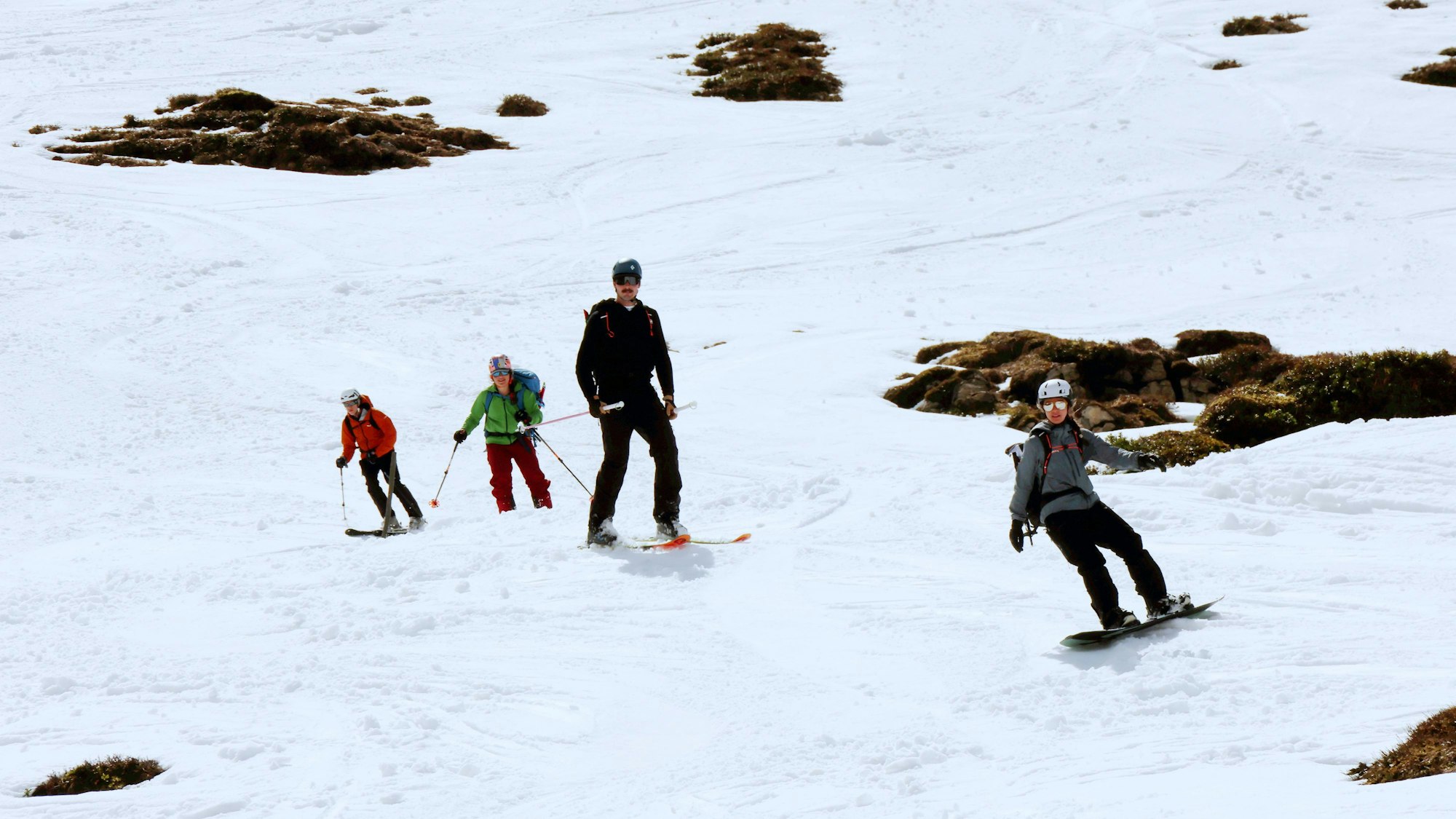Vier Personen auf Skiern und Snowboard im Schnee