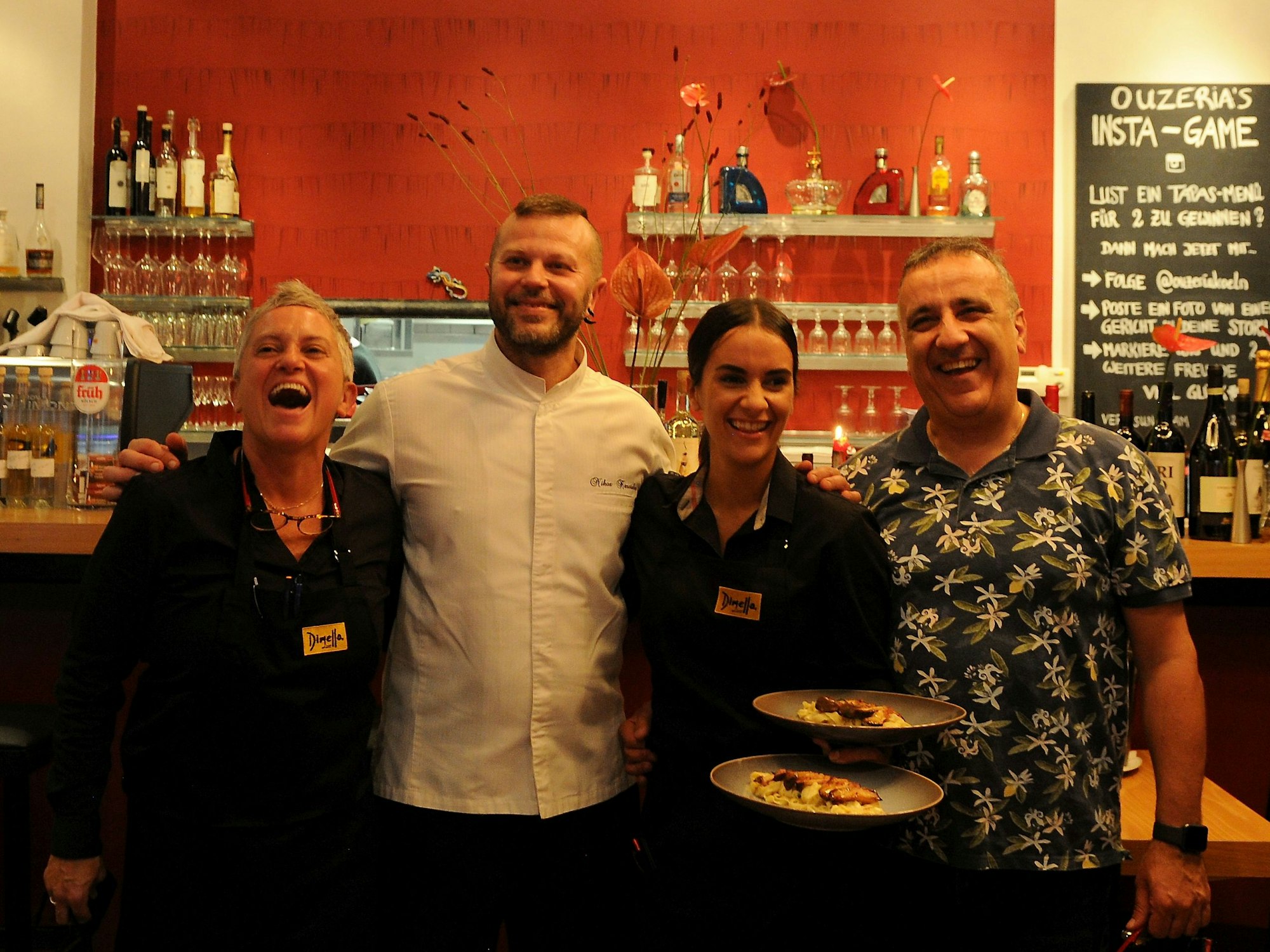 Zwei Frauen und zwei Männer stehen an der Theke eines Restaurants, eine der Frauen hält zwei angerichtete Teller in der Hand.