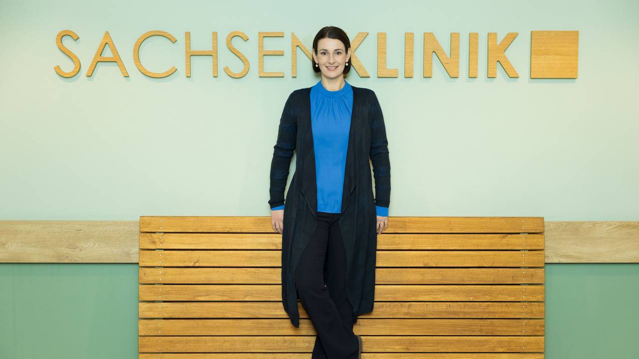 Schauspielerin Annett Renneberg steht vor einer Wand mit dem Schriftzug Sachsenklinik.