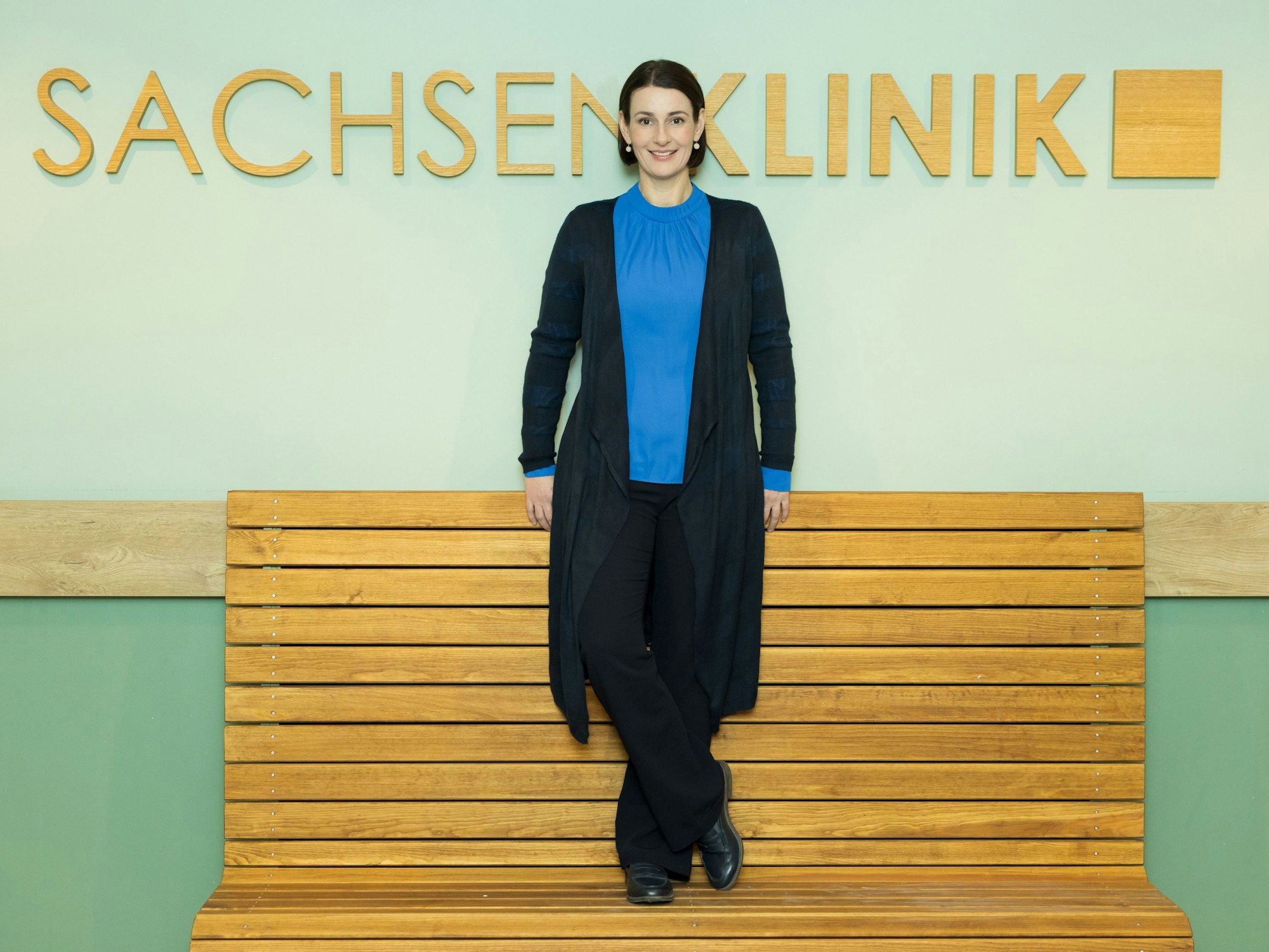 Schauspielerin Annett Renneberg steht vor einer Wand mit dem Schriftzug Sachsenklinik.