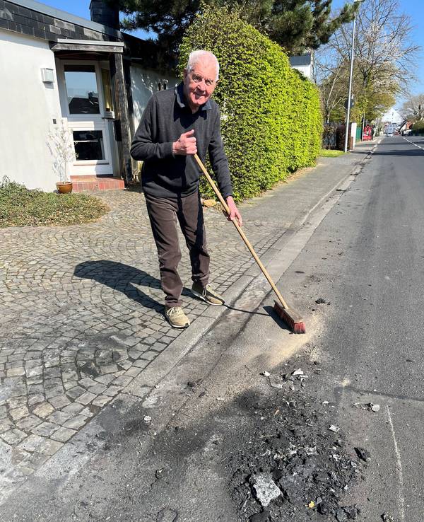 Ein älterer Mann steht mit einem Besen an der Straße.