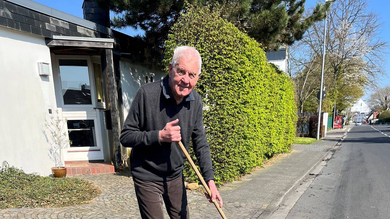 Ein älterer Mann steht mit einem Besen an der Straße.