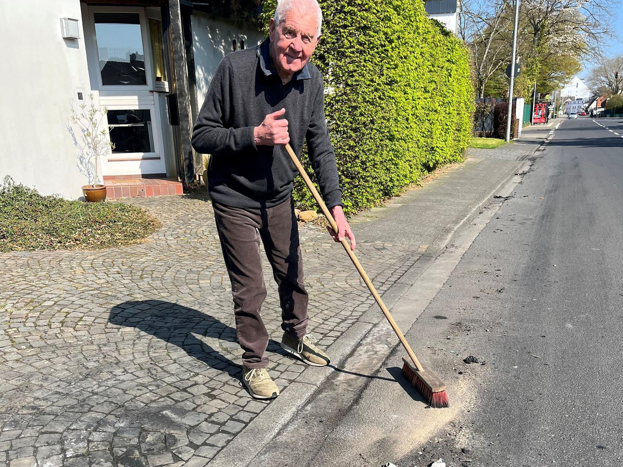 Ein älterer Mann steht mit einem Besen an der Straße.