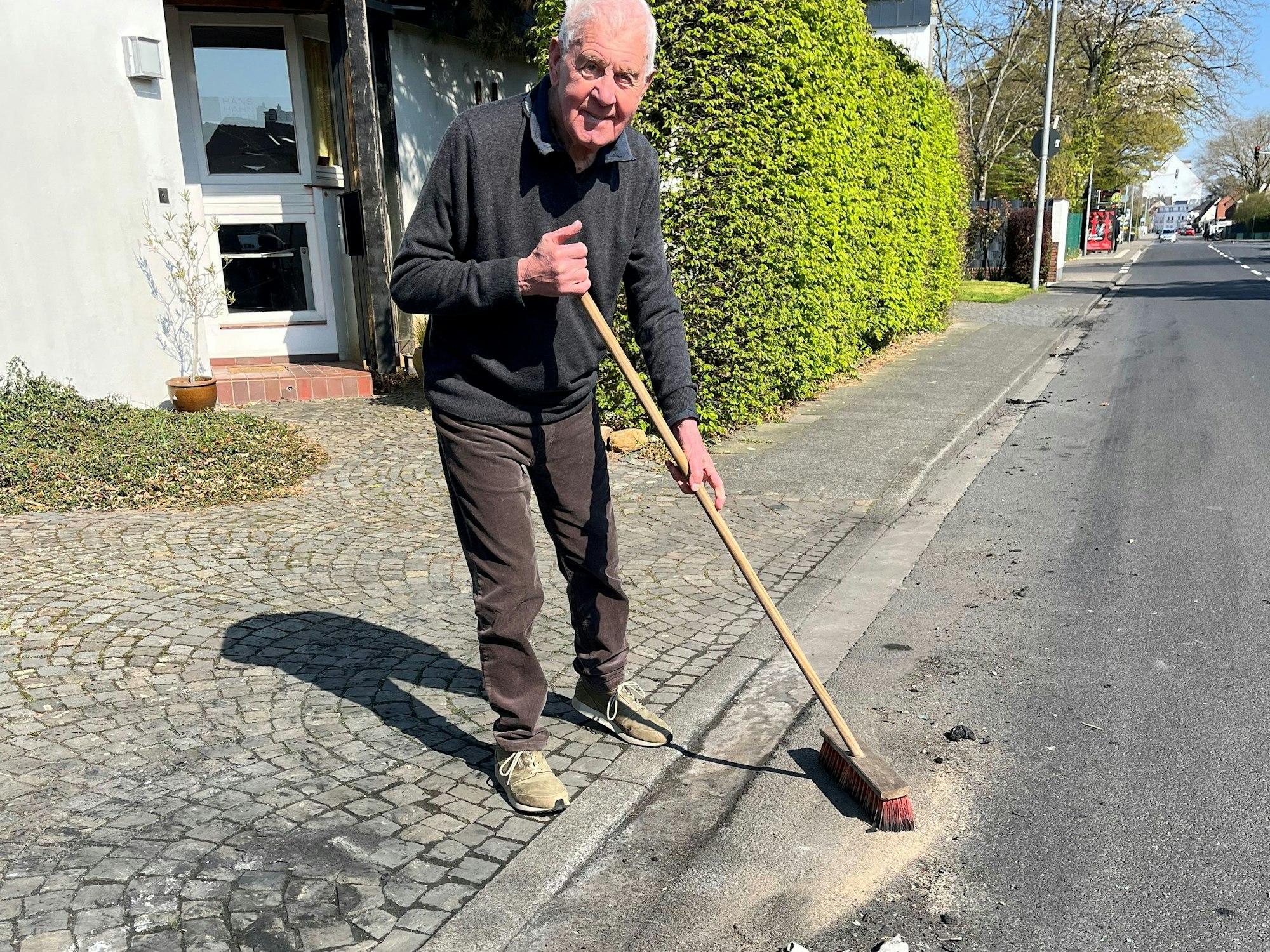 Ein älterer Mann steht mit einem Besen an der Straße.