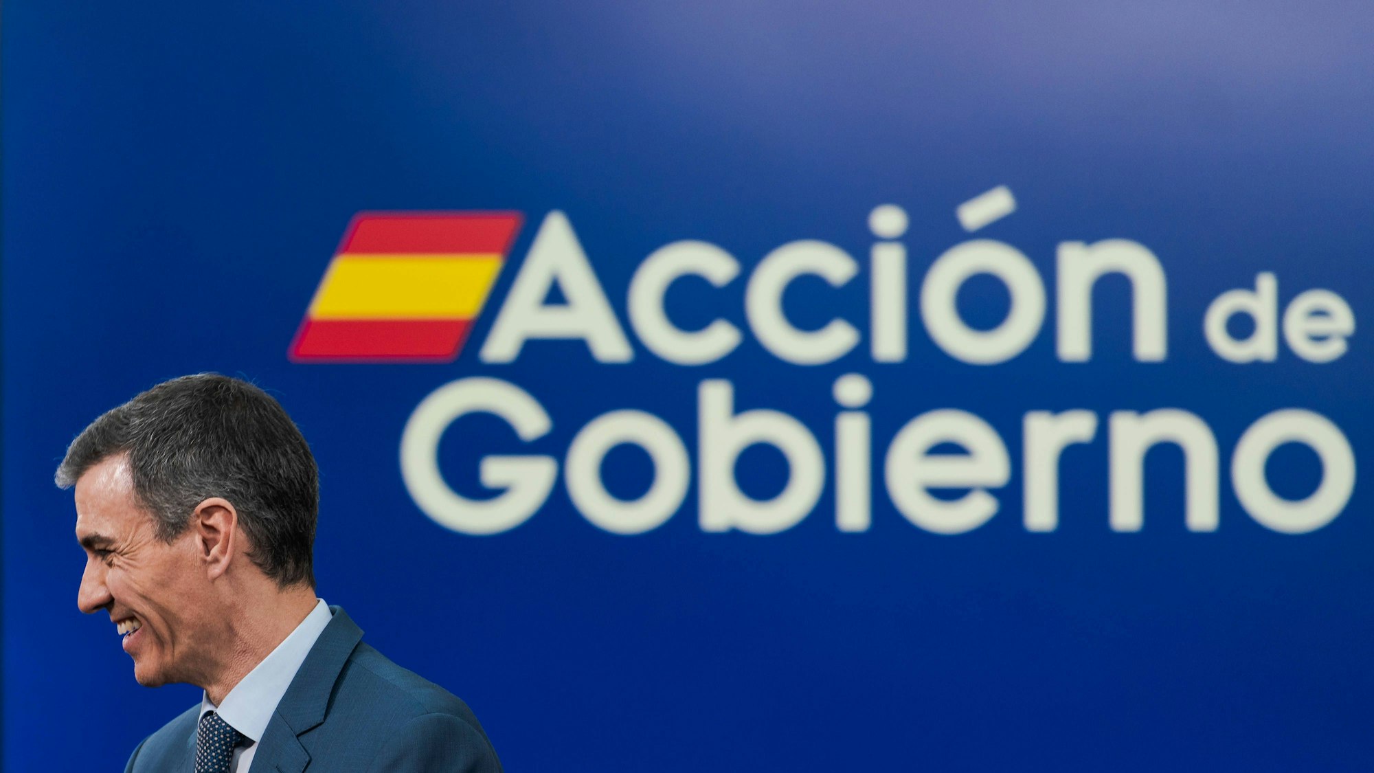 Pedro Sánchez lächelt vor blauem Banner