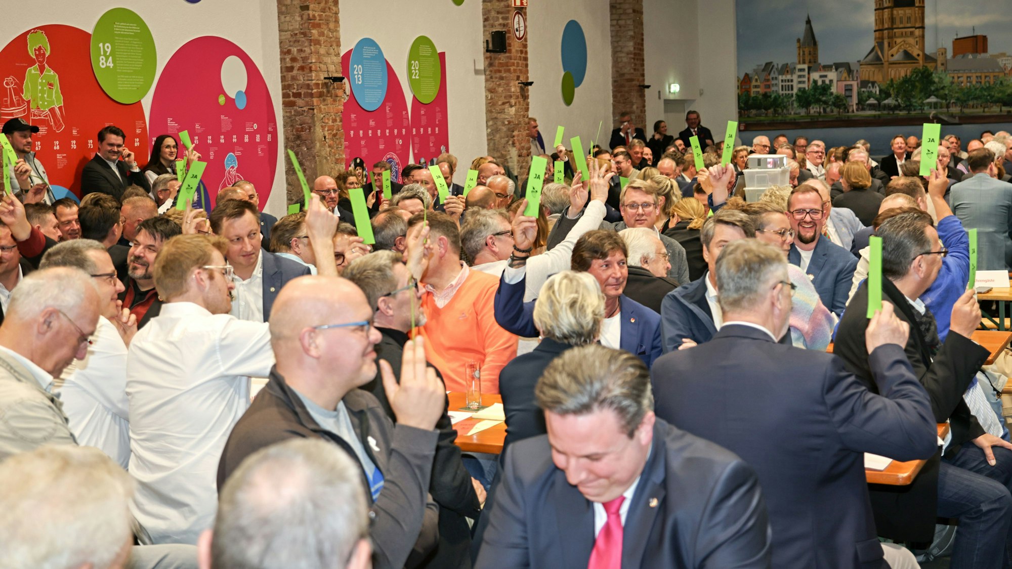 Mitglieder heben die Abstimmungskarten in die Höhe.