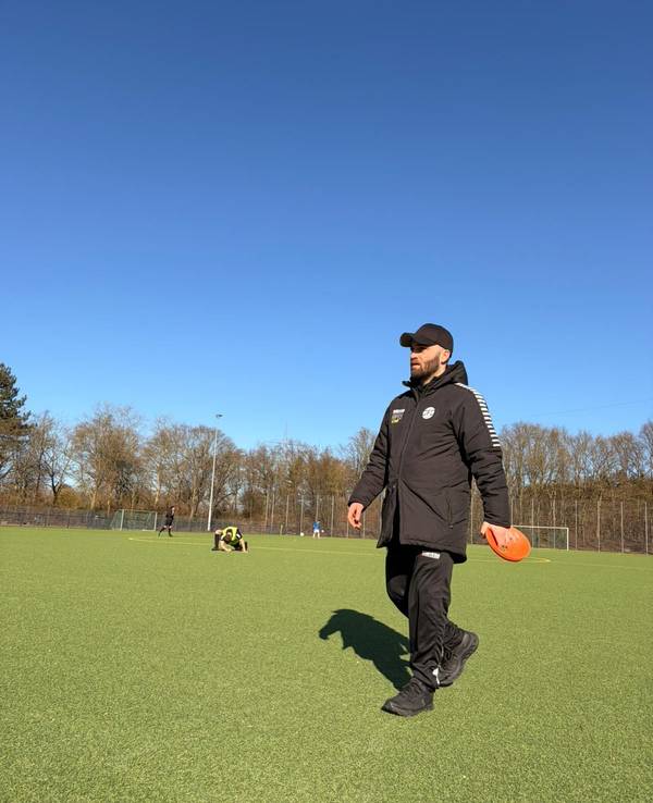 Ein Mann geht in Sportkleidung über einen Fußballplatz.