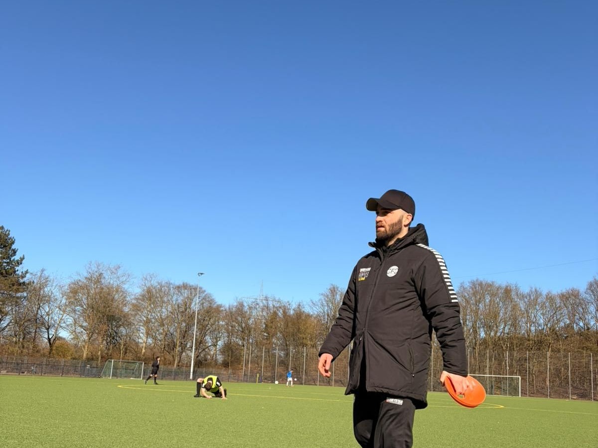 Ein Mann geht in Sportkleidung über einen Fußballplatz.