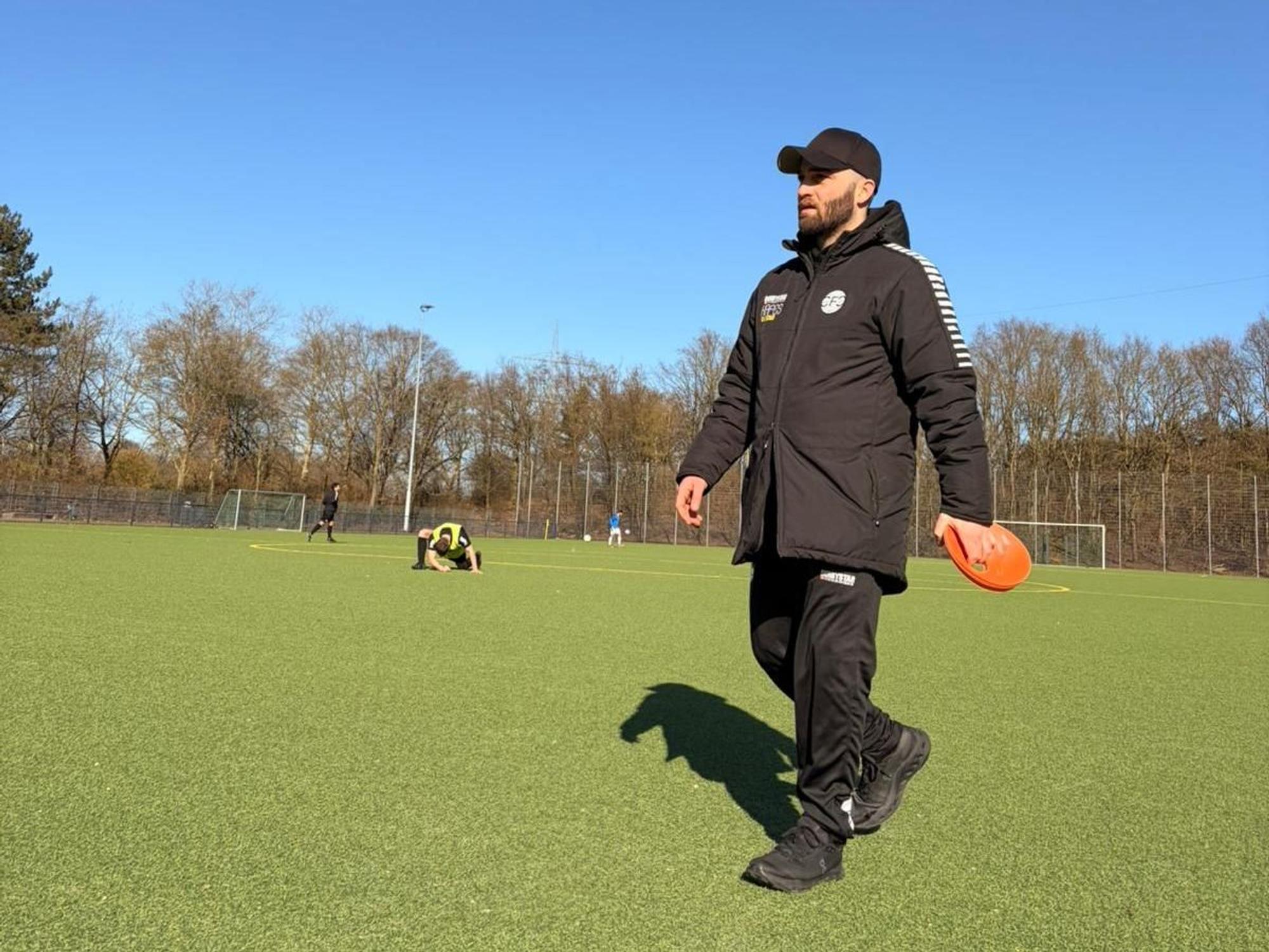 Ein Mann geht in Sportkleidung über einen Fußballplatz.