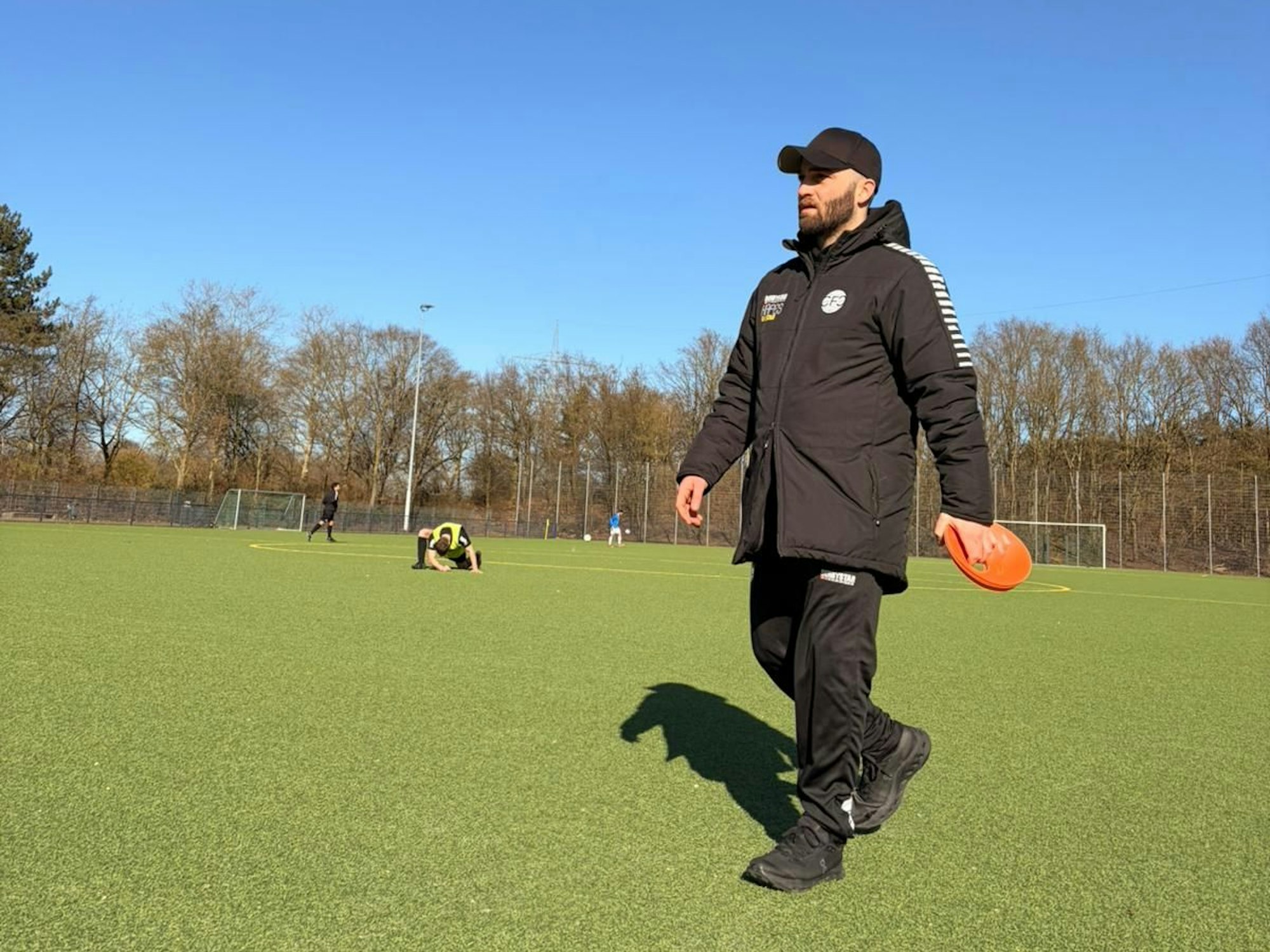 Ein Mann geht in Sportkleidung über einen Fußballplatz.