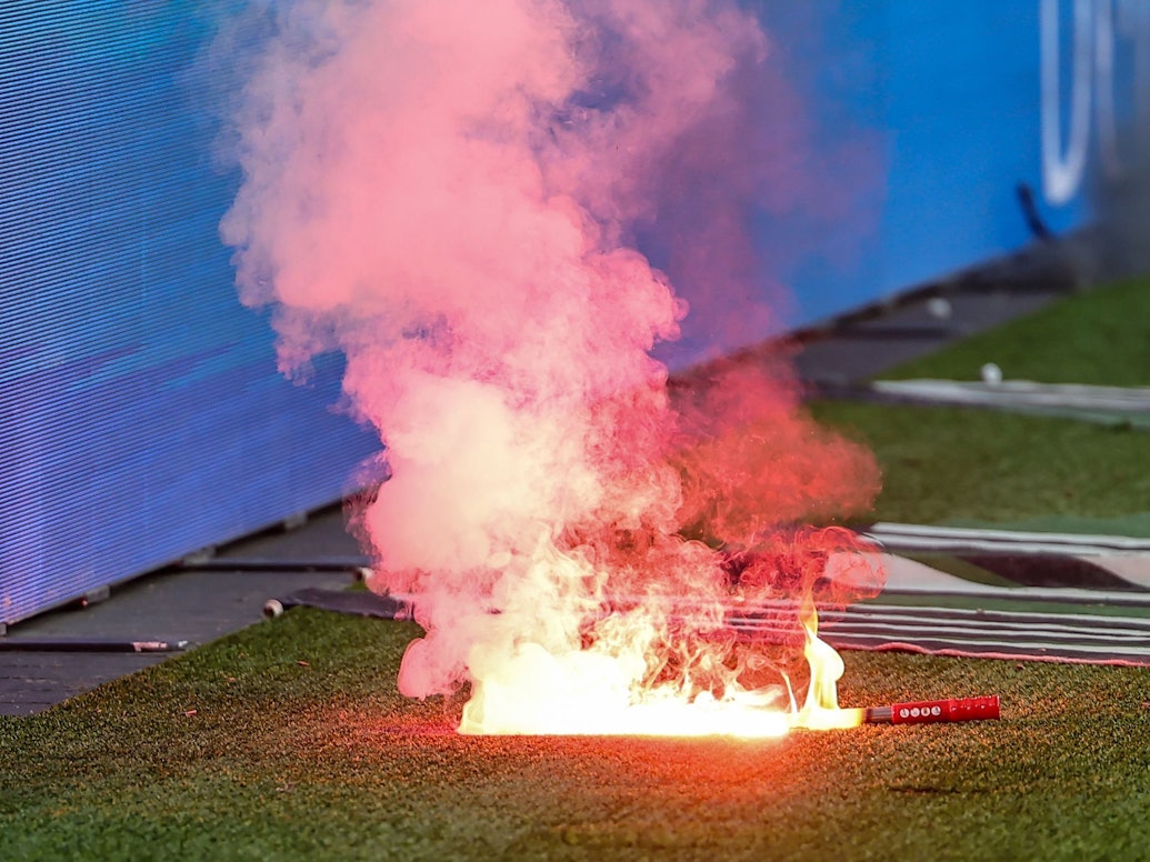Eine Leuchtfackeln brennt an einem Fußballplatz.