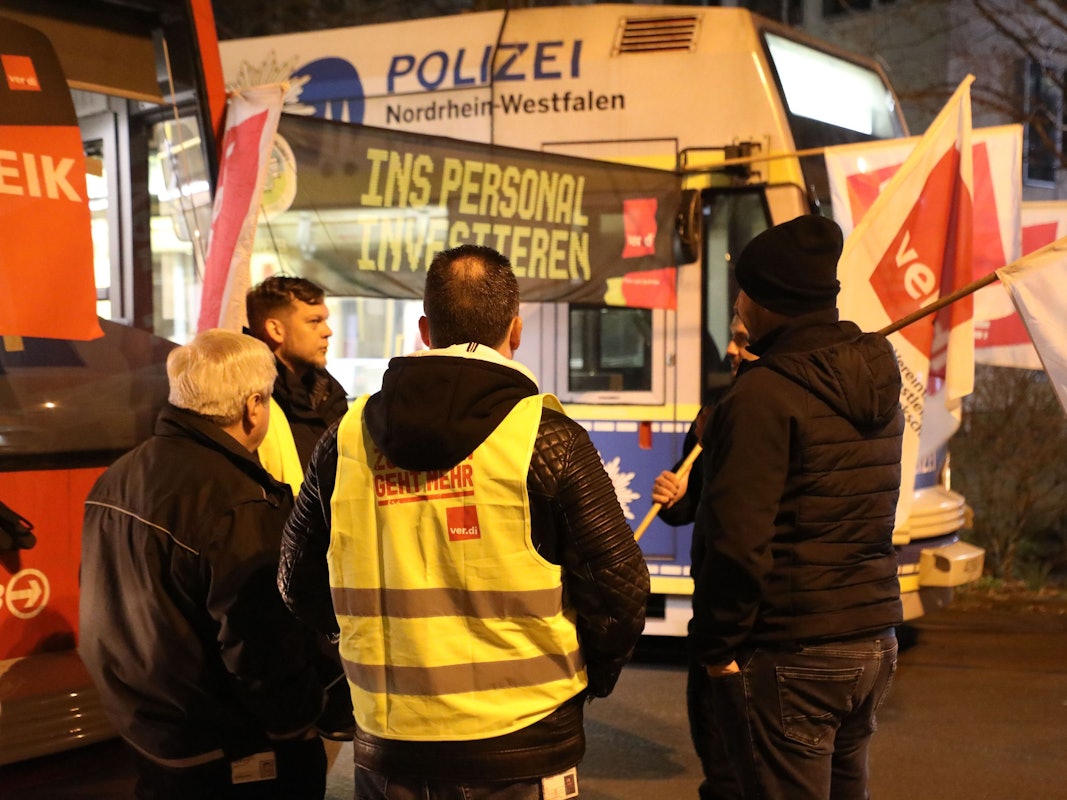 Streikende stehen mit Flaggen vor parkenden Stadtbahnen der KVB. In der Tarifrunde für den kommunalen Nahverkehr hatte Verdi für Montag zu Warnstreiks aufgerufen.