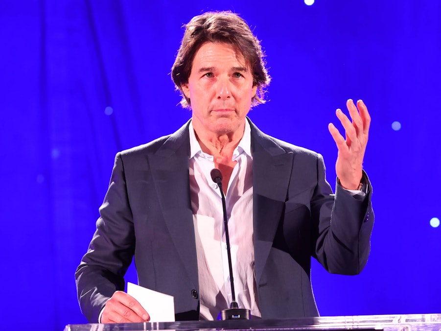 Tom Cruise spricht an einem Pult vor blauem Hintergrund