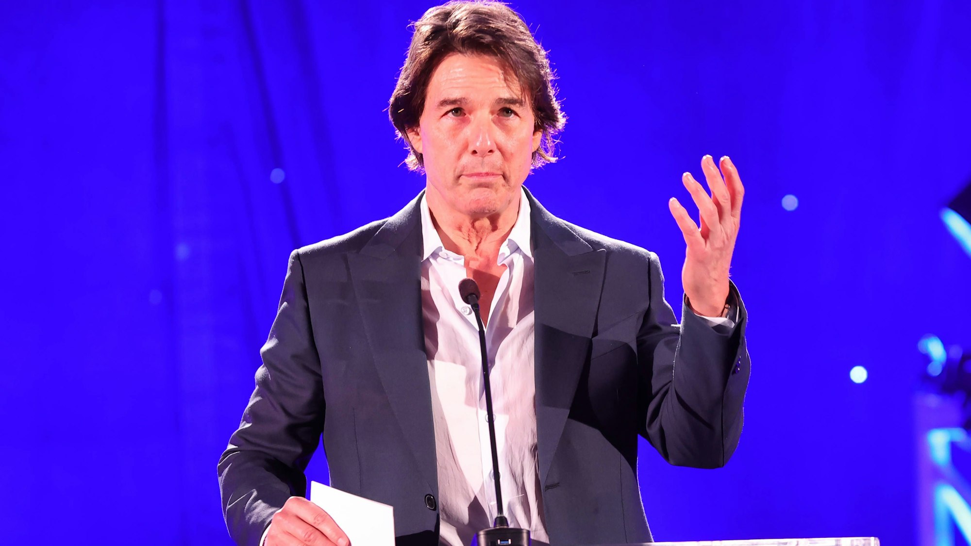 Tom Cruise spricht an einem Pult vor blauem Hintergrund