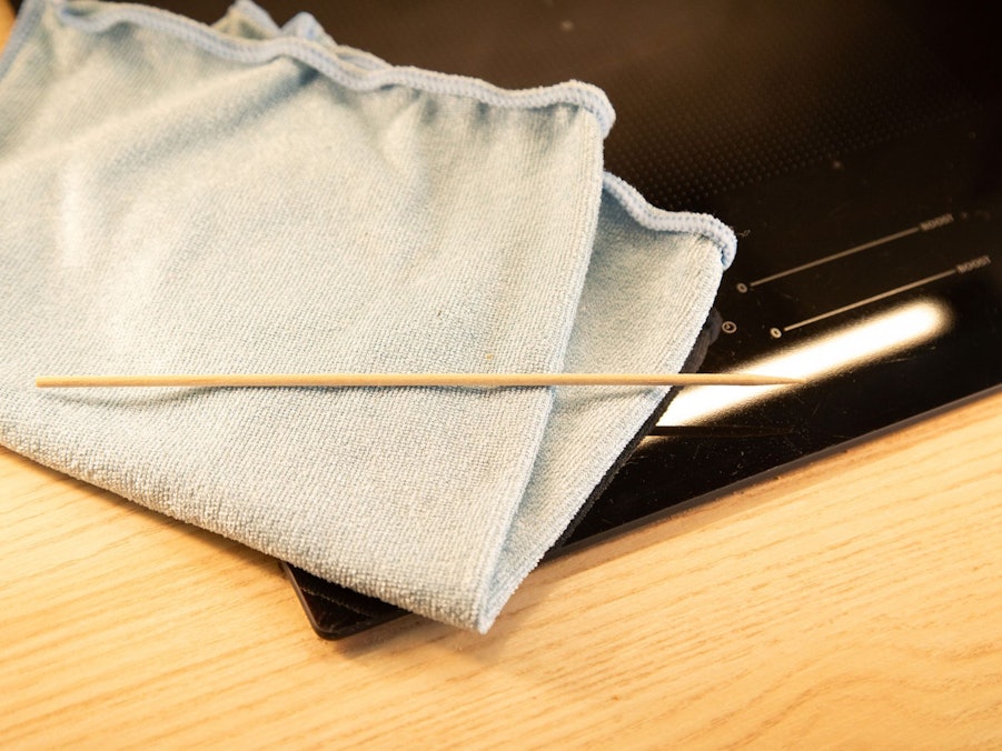 Ein Holzspieß und ein Mikrofasertuch liegen neben einem Kochfeld