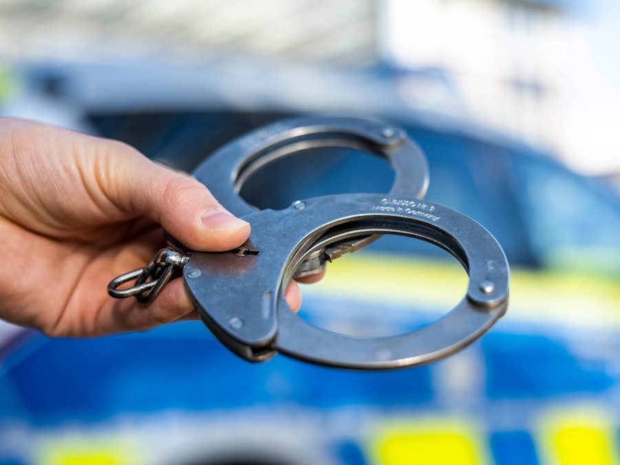 Handschellen vor Polizeiwagen - Symbolbild