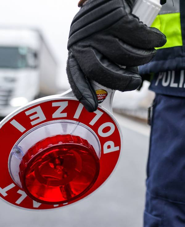 Ein Polizist hält eine Halt-Kelle in der Hand, ein Lkw kommt auf ihn zu.
