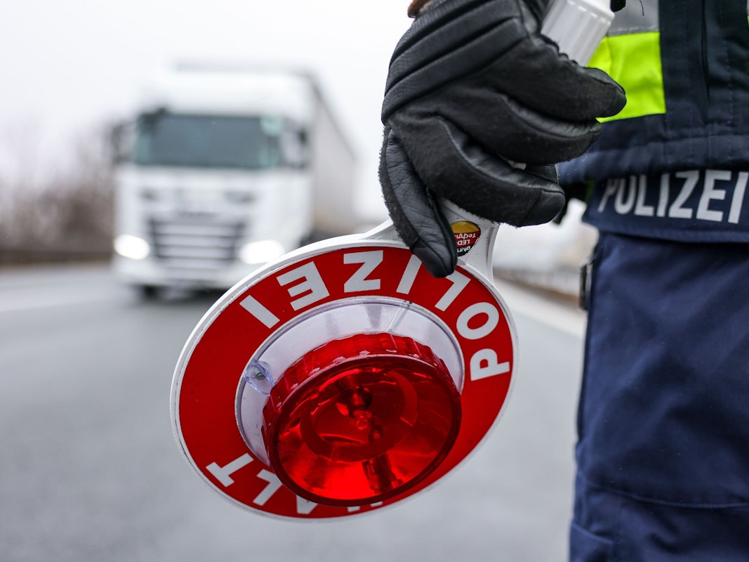 Ein Polizist hält eine Halt-Kelle in der Hand, ein Lkw kommt auf ihn zu.