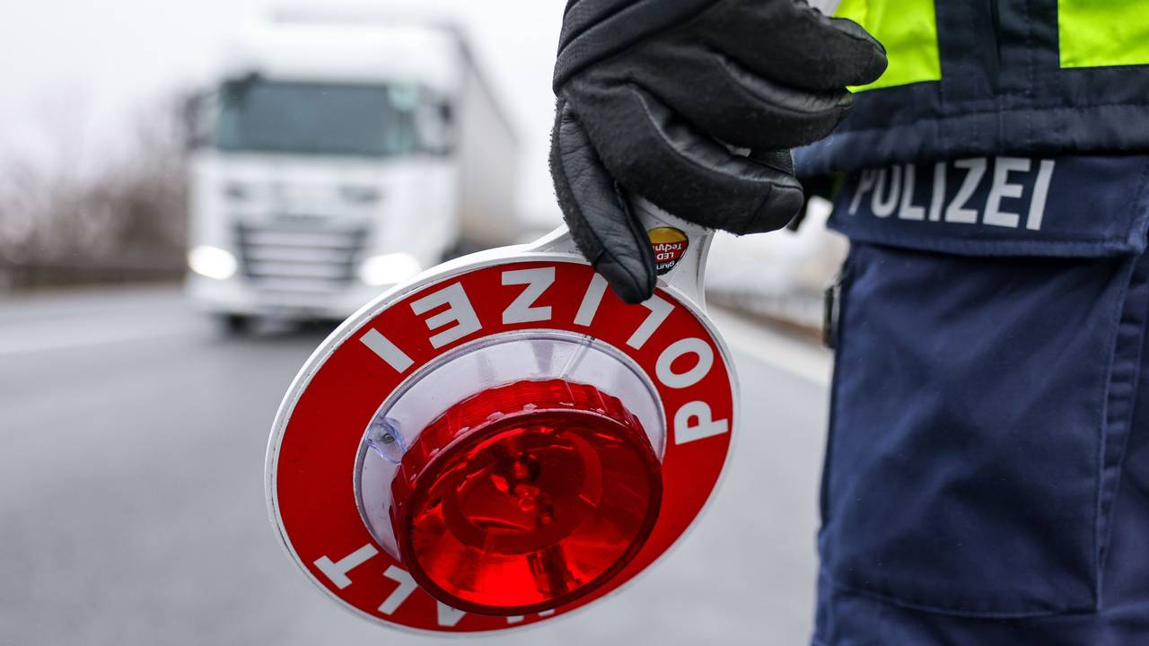 Ein Polizist hält eine Halt-Kelle in der Hand, ein Lkw kommt auf ihn zu.