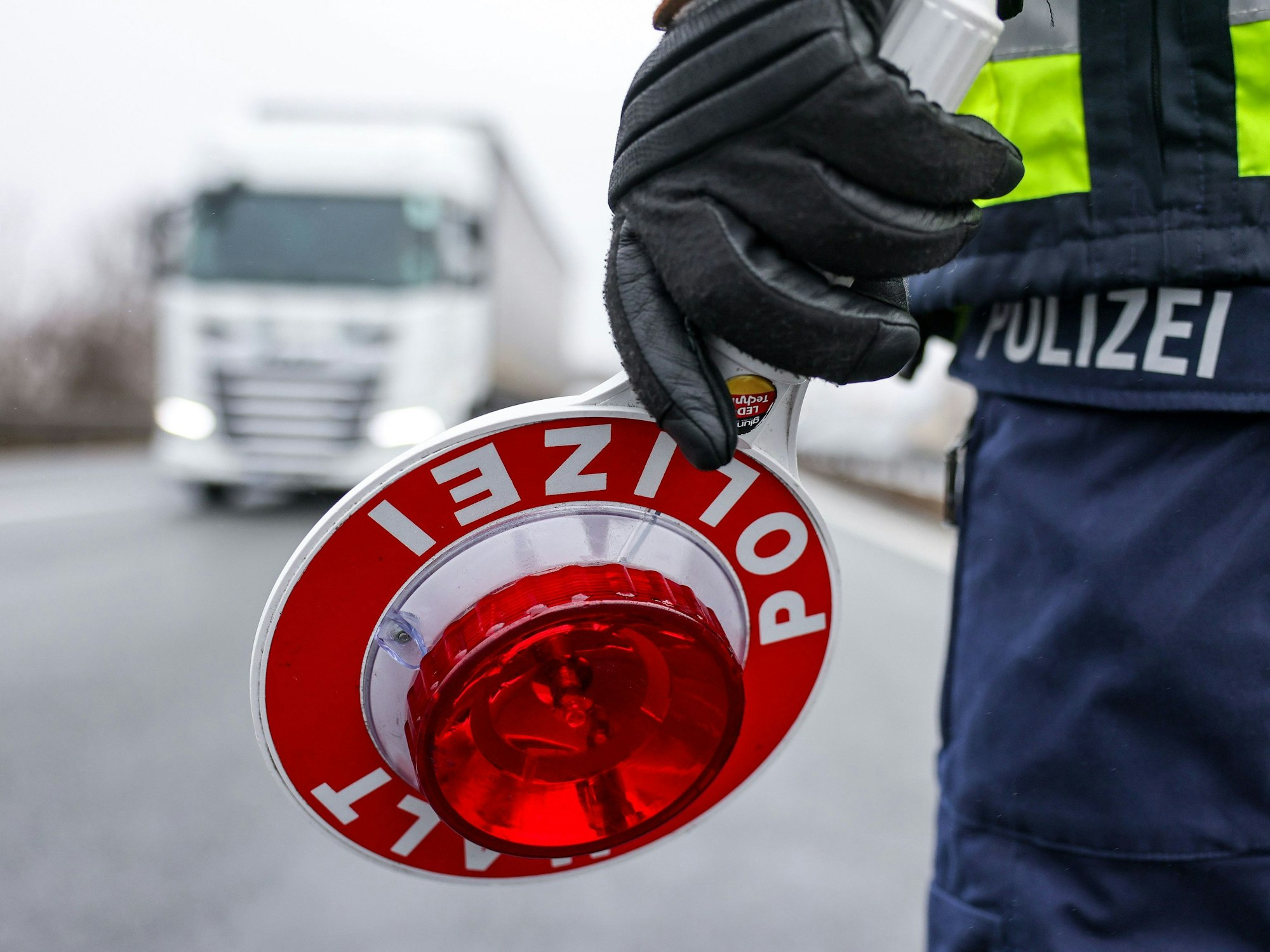 Ein Polizist hält eine Halt-Kelle in der Hand, ein Lkw kommt auf ihn zu.