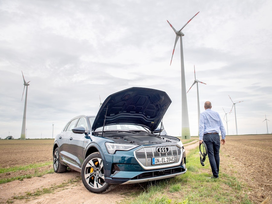 Ein Mann mit Ladekabel steht neben einem E-Auto im Windpark