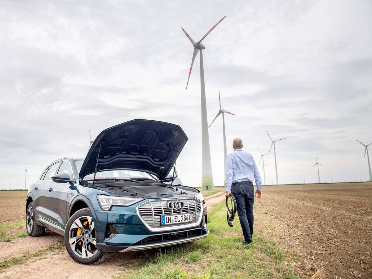 Ein Mann mit Ladekabel steht neben einem E-Auto im Windpark