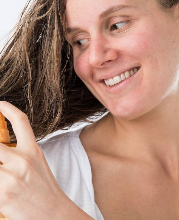 Eine Frau sprüht sich mit einem Haarpflegeprodukt auf die Haare