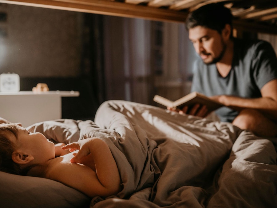 Vater liest seinen Kindern bei der Einschlafbegleitung etwas vor