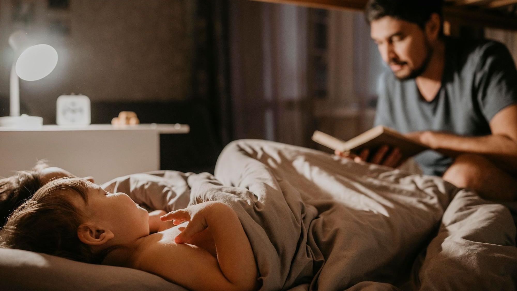 Vater liest seinen Kindern bei der Einschlafbegleitung etwas vor